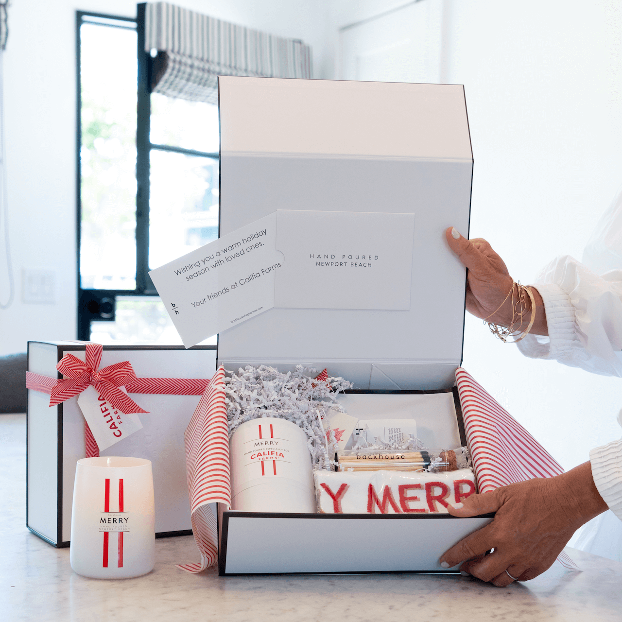 Person opening a gift box with festive items on a marble surface