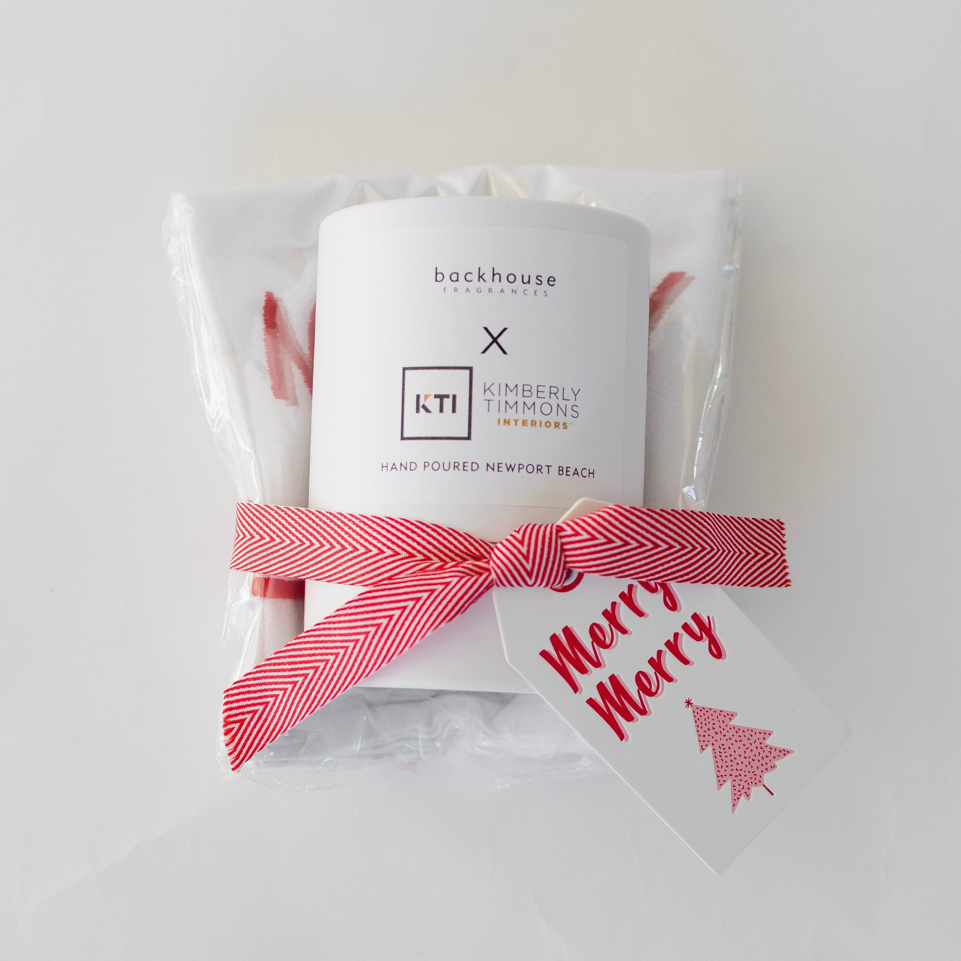 Candle with a red and white bow and 'Merry' tag on a light gray background