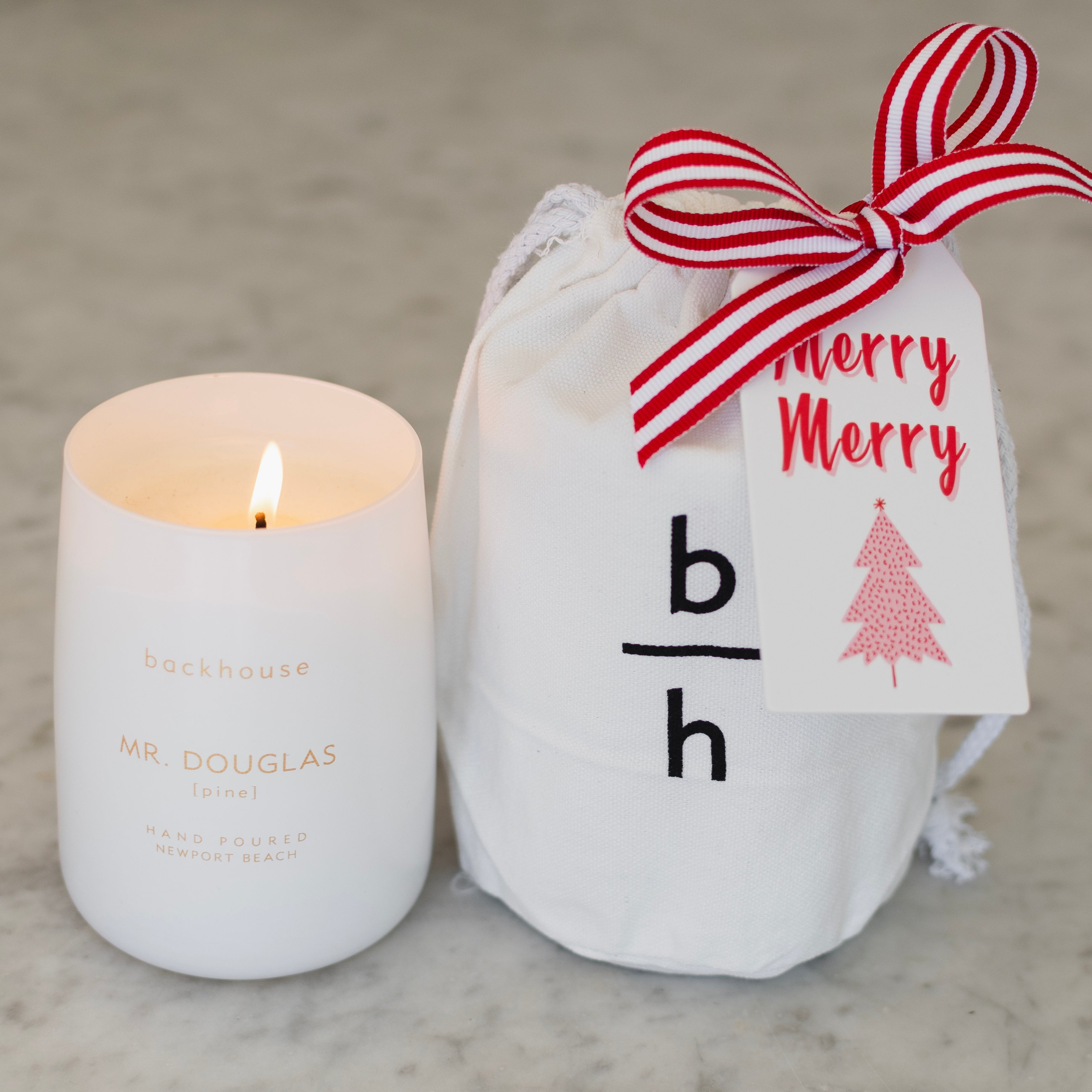 White candle and white drawstring bag with red and white ribbon on a light gray surface