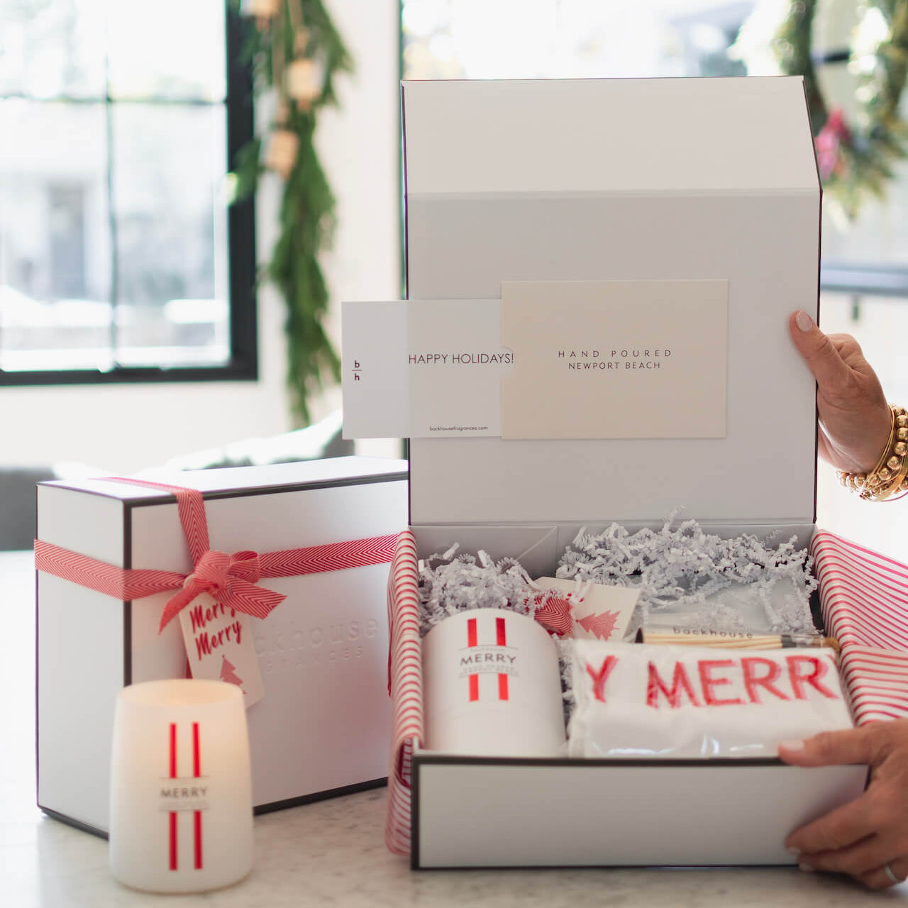Gift box with 'Happy Holidays' card, candles, and other items on a table.