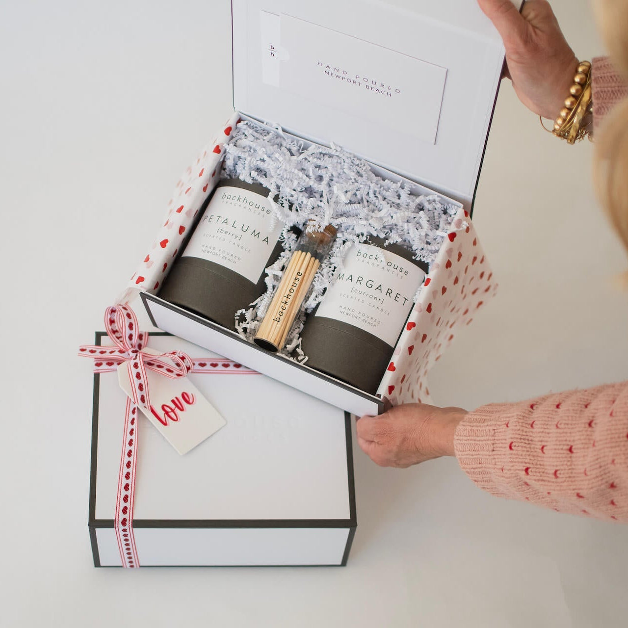 Gift set with candles and matches in a decorative box, held by a person wearing a pink sweater.