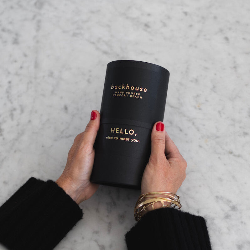 Person holding a black candle labeled 'backhouse' on a marble surface