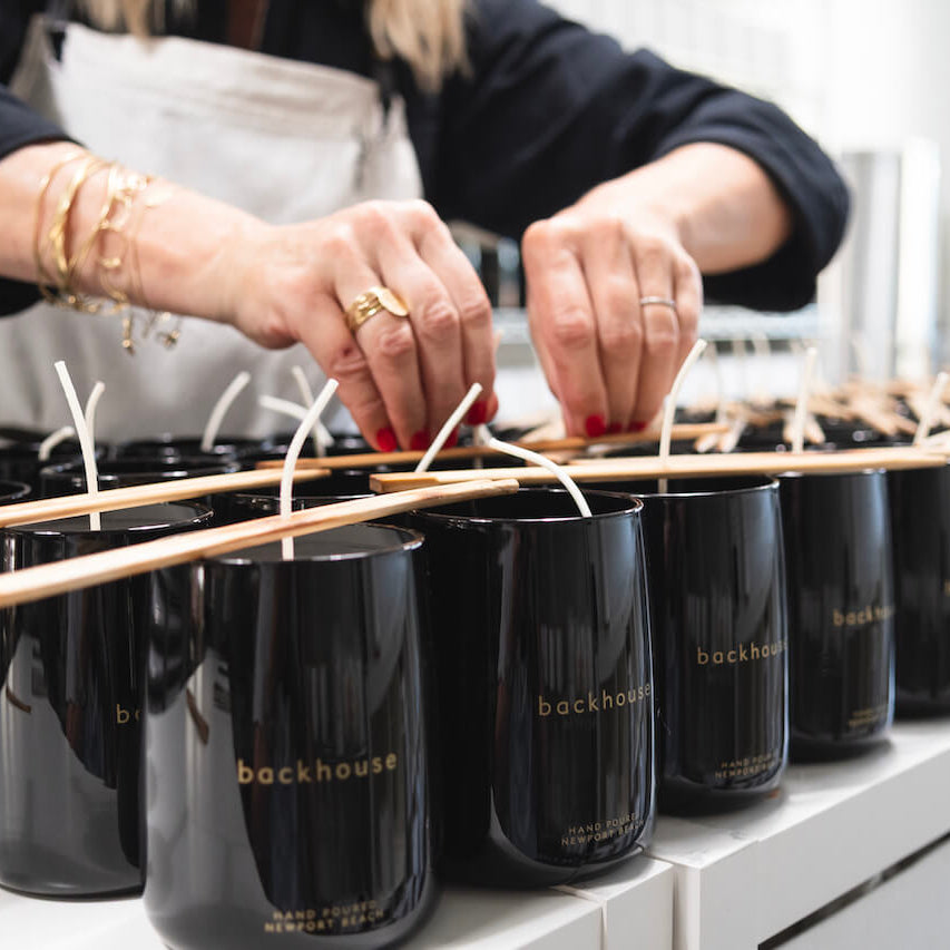 Person arranging candles in black containers with 'backhouse' branding.