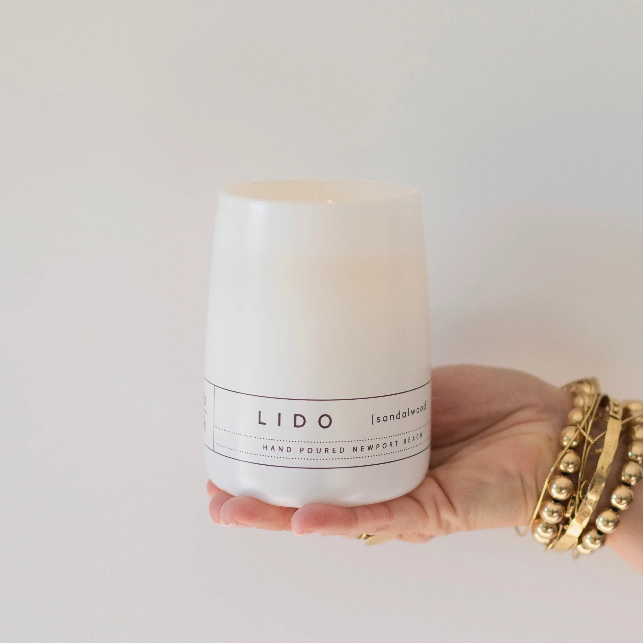 Hand holding the Lido sandalwood hurricane candle by backhouse against a white background in its classic glass vessel.