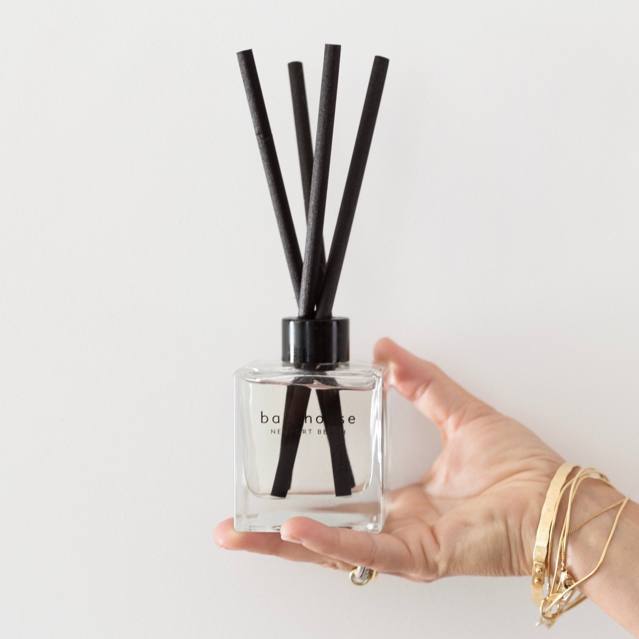 Backhouse Newport Beach LIDO reed diffuser held in hand to show size, sandalwood scent in a clear glass bottle with black reeds.