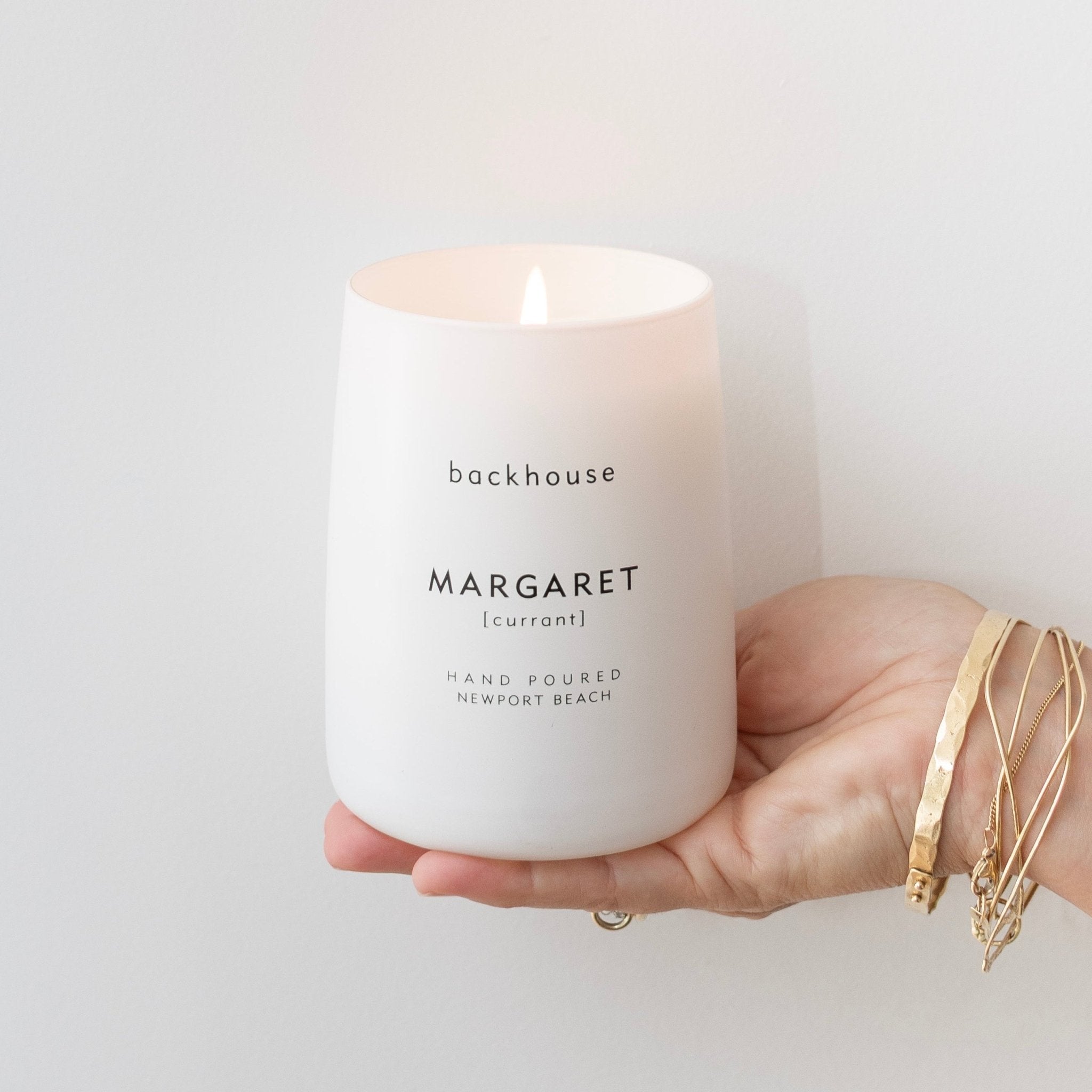 Hand holding lit Backhouse Fragrances Margaret currant scented candle, hand-poured luxury home fragrance in Newport Beach California