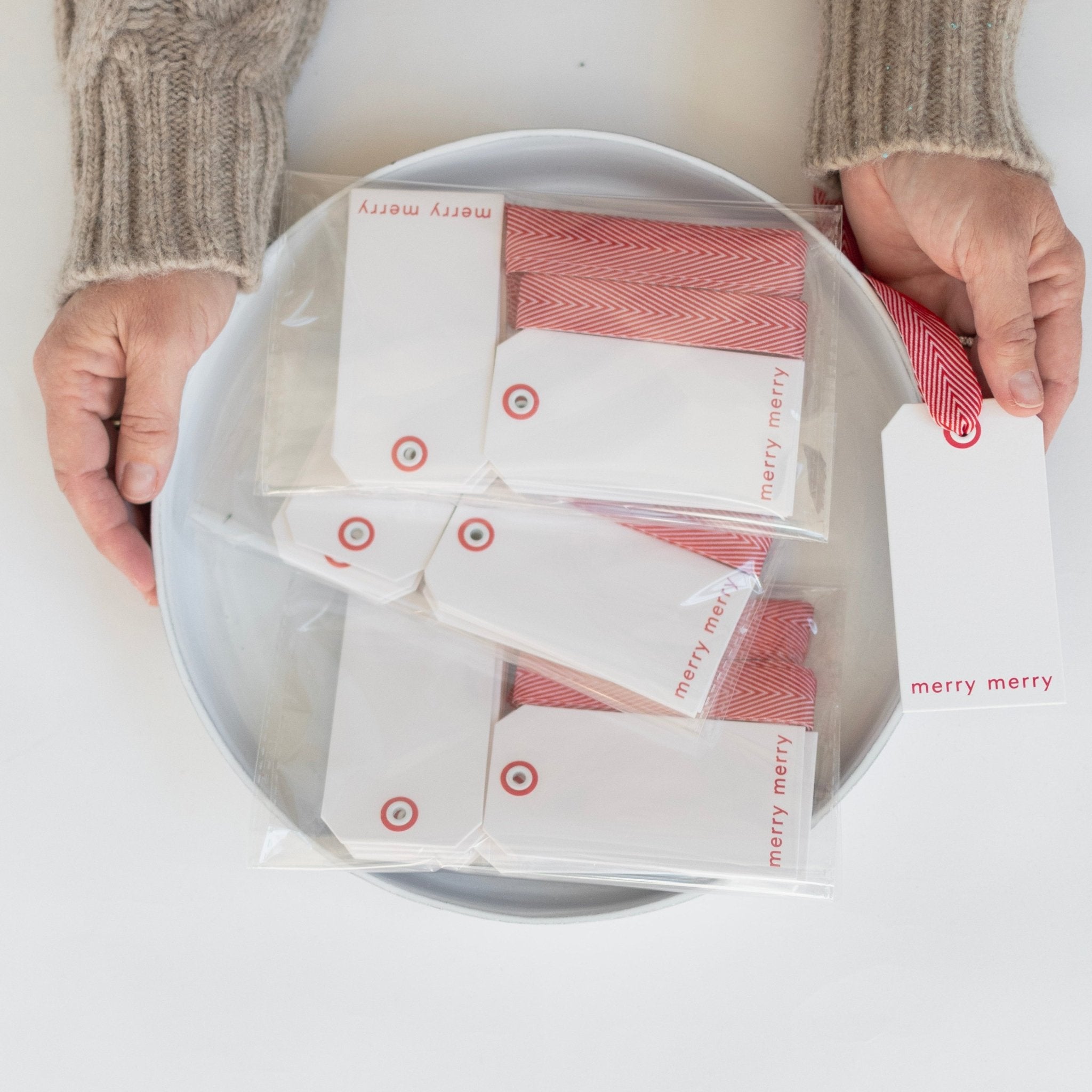 Merry merry hangtags displayed on a platter with a person holding a hangtag in their hand. Gifting hangtags.