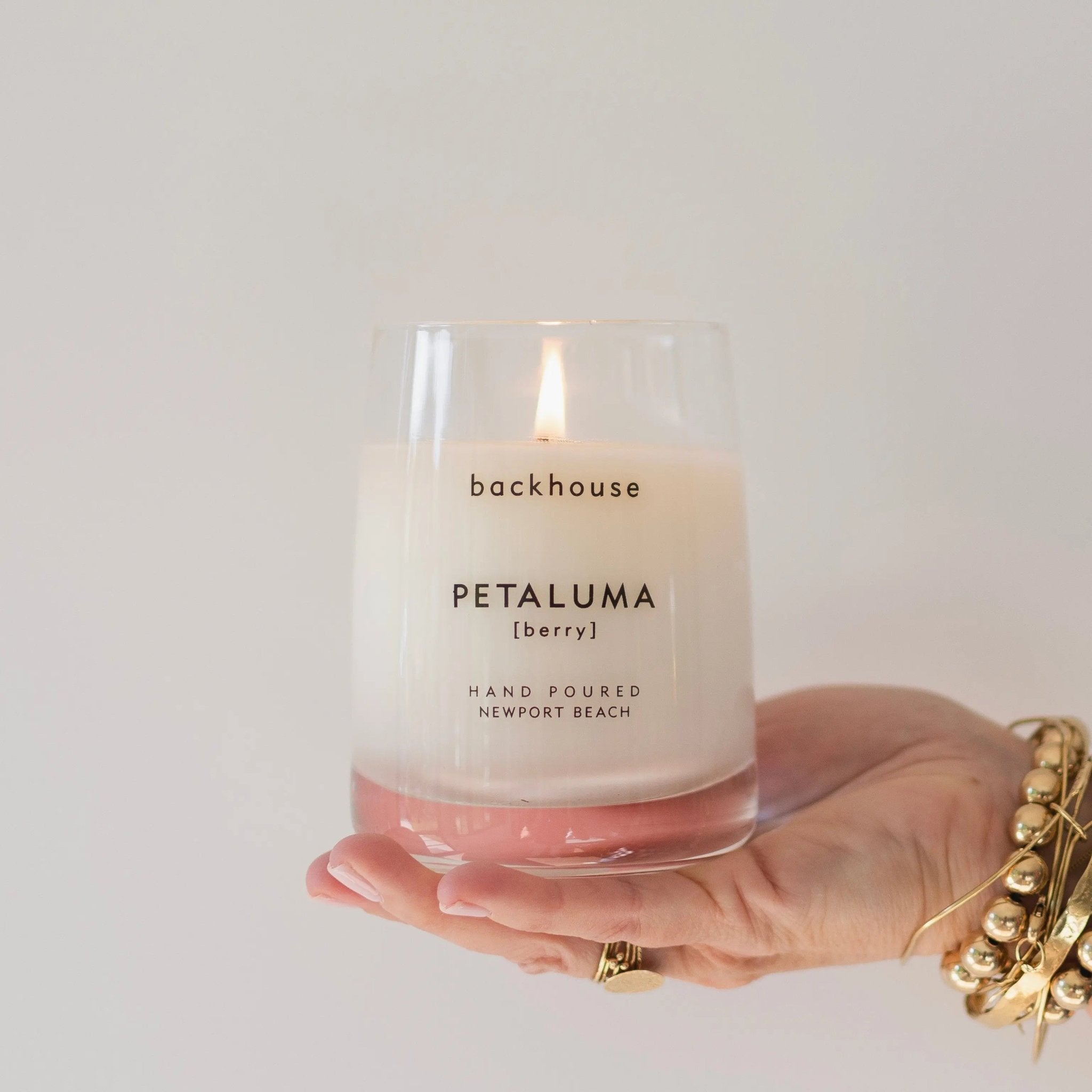 Hand holding the Petaluma berry candle by backhouse against a white background, shown in its classic glass vessel.