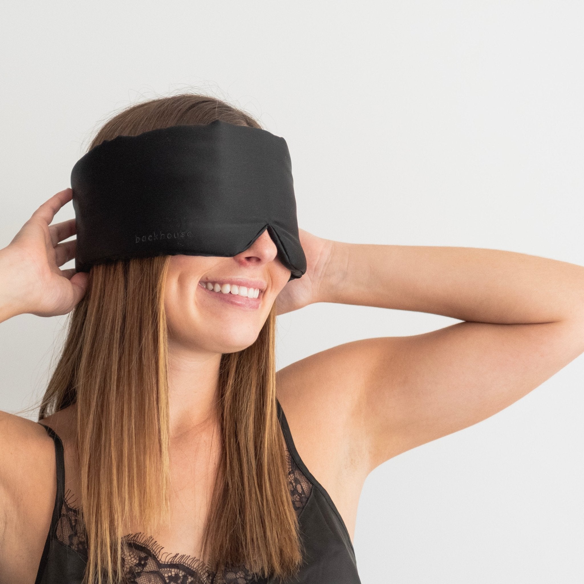 Woman wearing the black silk eye mask by backhouse against a white background.
