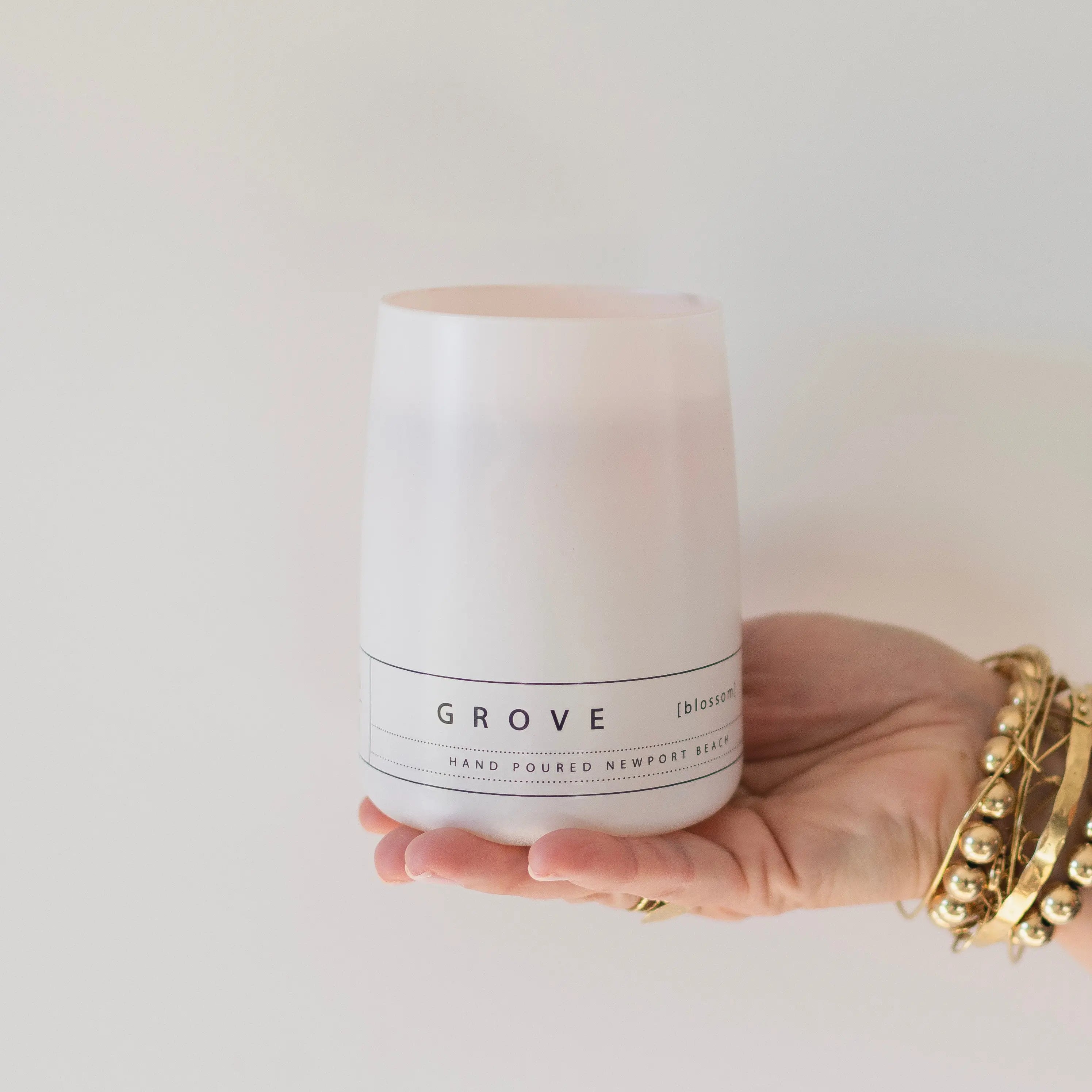 Hand holding the Grove orange blossom candle by backhouse against a white background in its classic glass vessel.