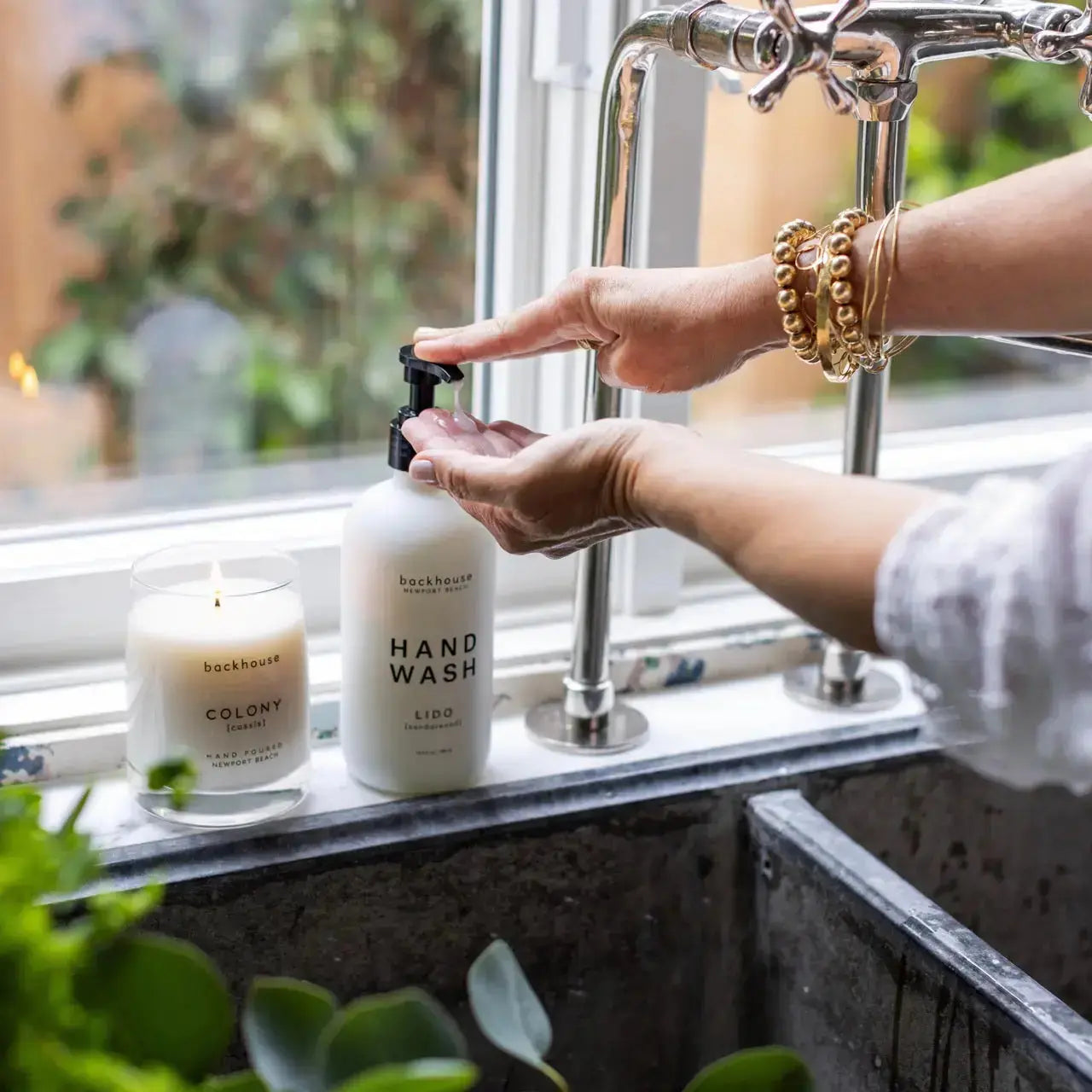 Hands using the Lido sandalwood hand wash by backhouse at a kitchen sink beside a lit candle.