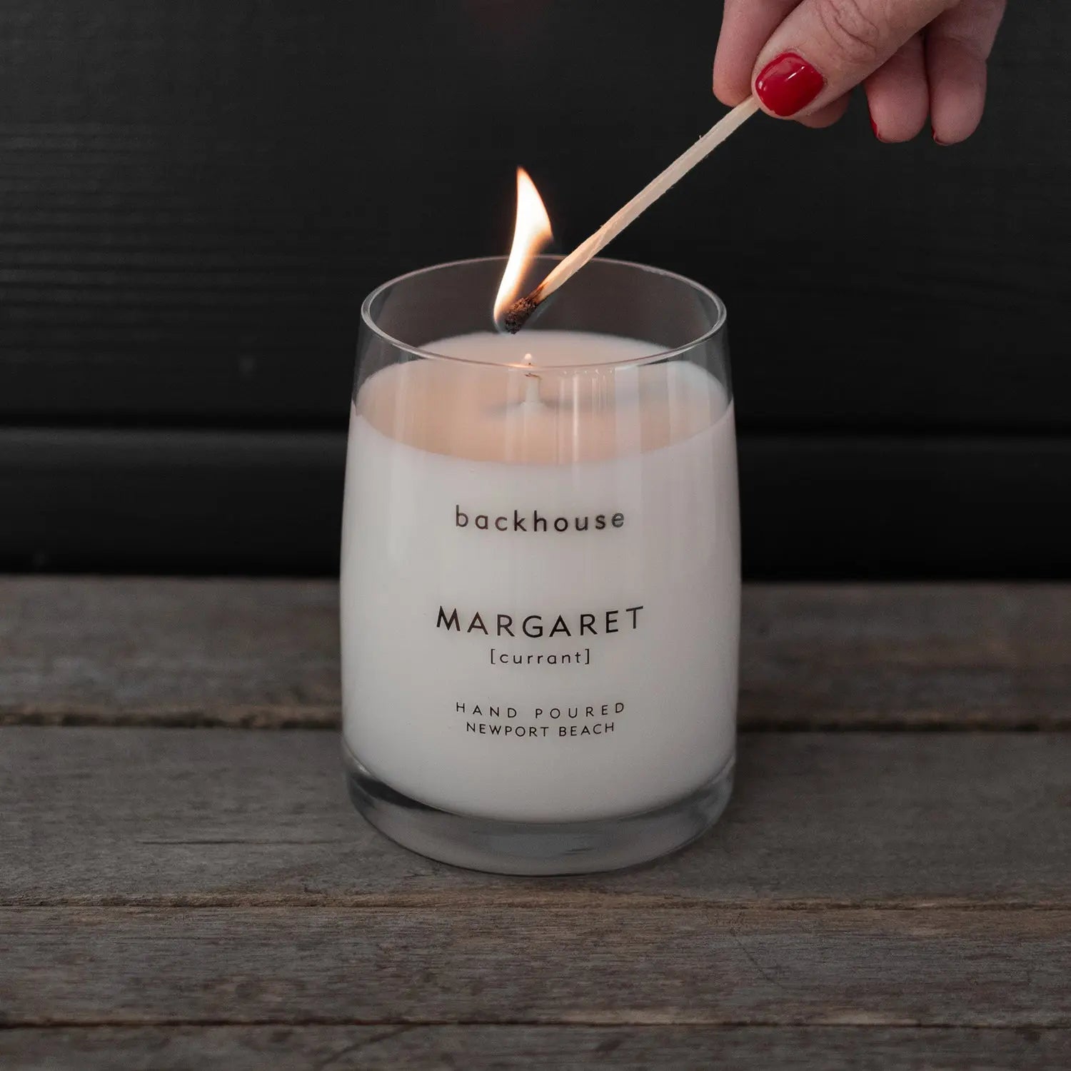 Hand lighting the Margaret currant candle by backhouse against a dark background.
