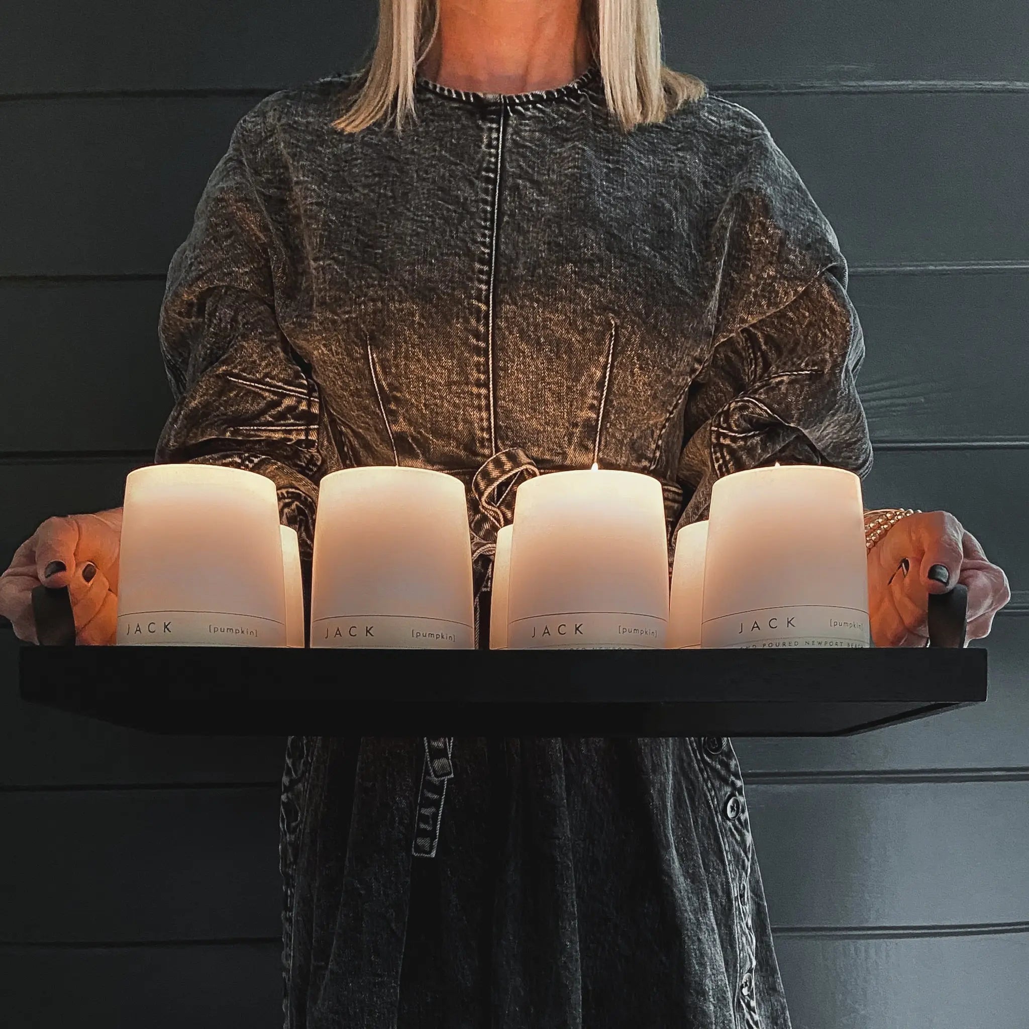 Multiple Jack pumpkin candles by backhouse lit and held in hand against a dark background.