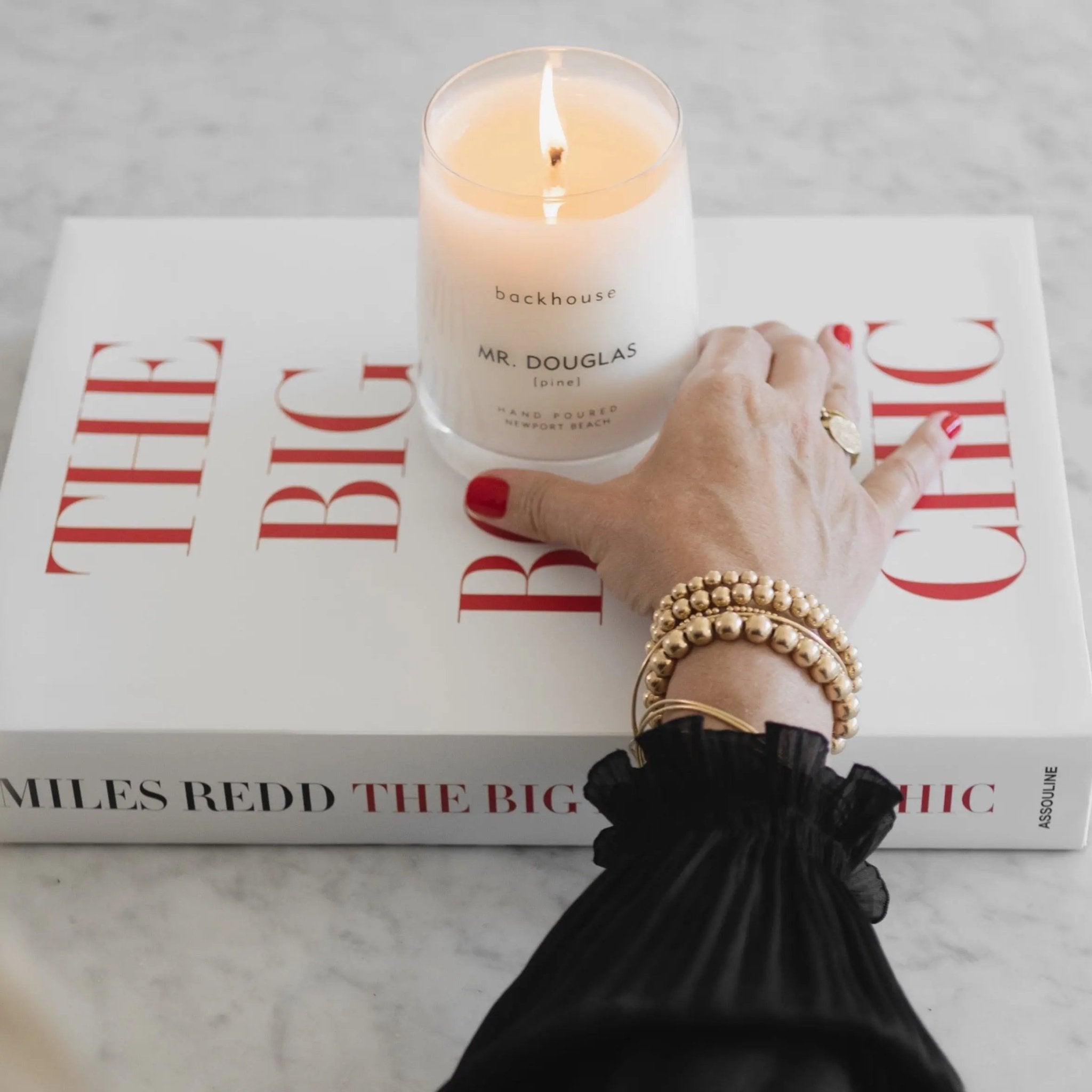 Mr. Douglas pine candle by backhouse burning on a red and white coffee table book.