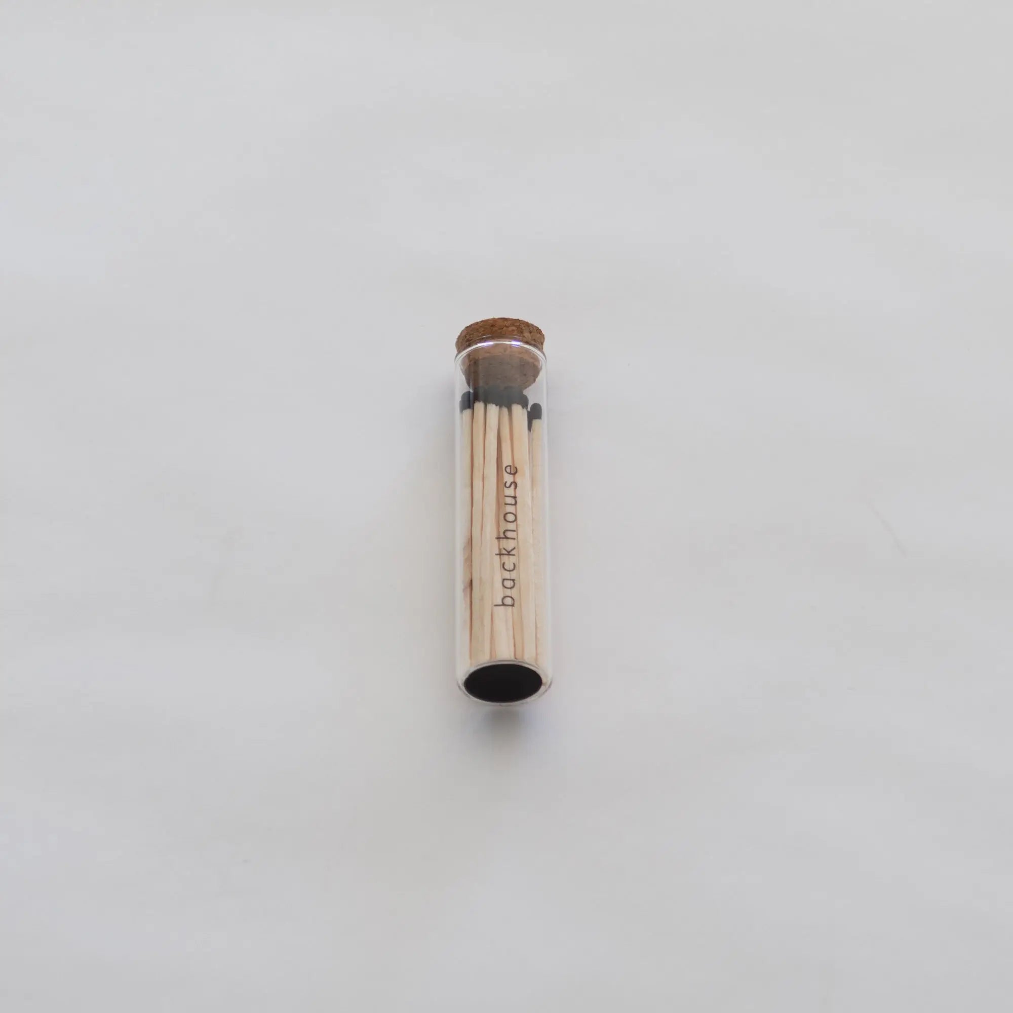 Glass tube of matches by backhouse displayed against a white background.