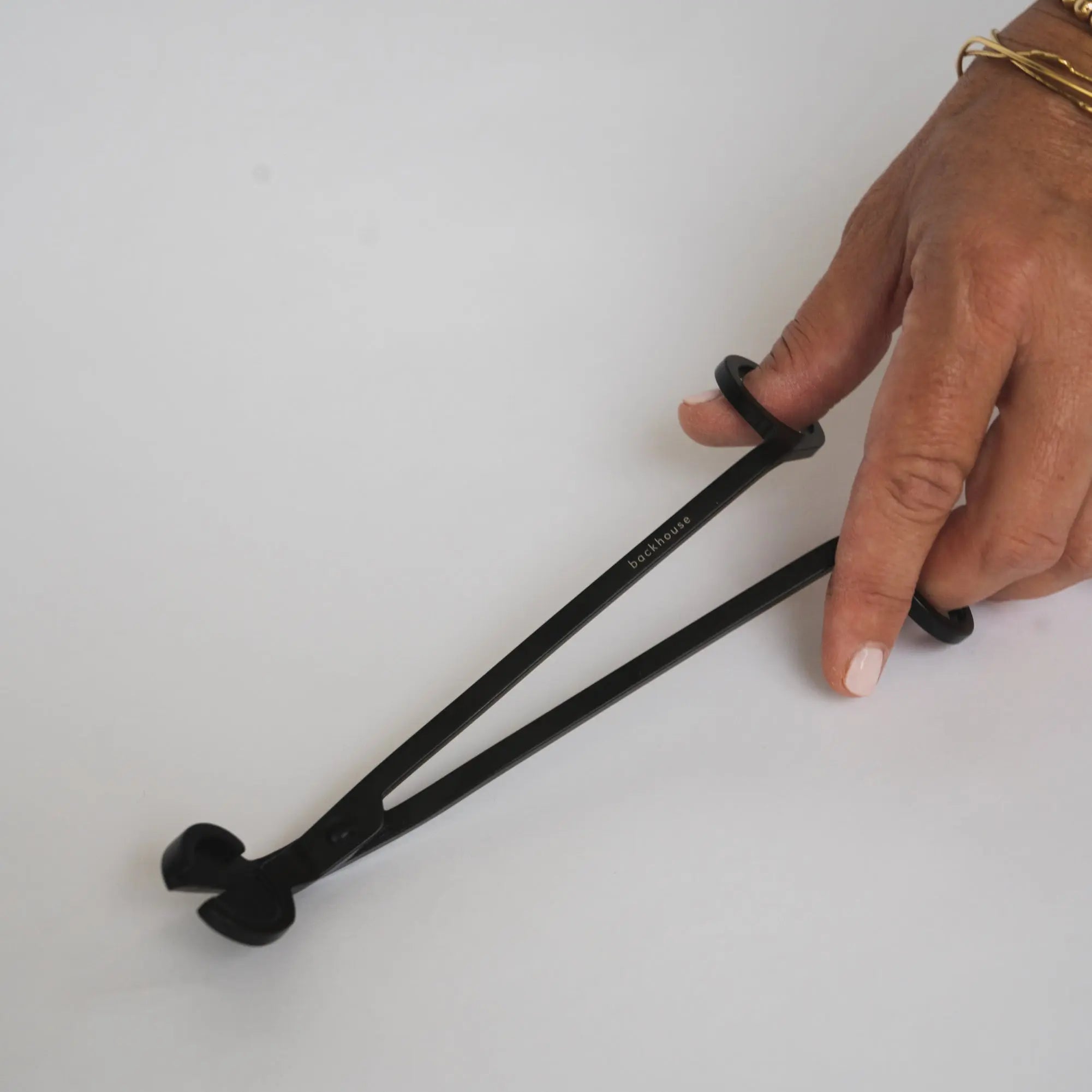 Hand holding the black wick trimmer by backhouse against a white background.