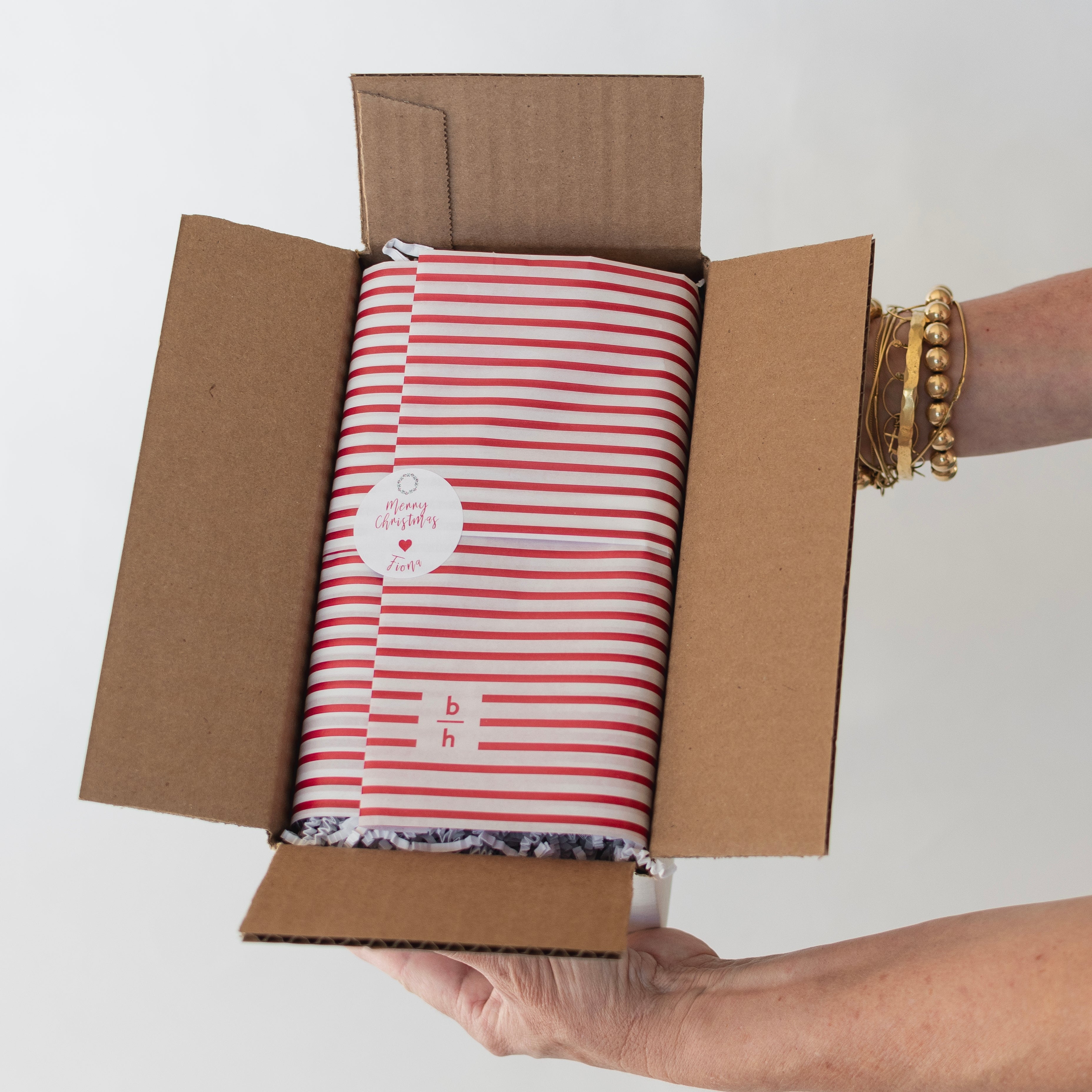 Person holding a cardboard box with a red and white striped product inside.