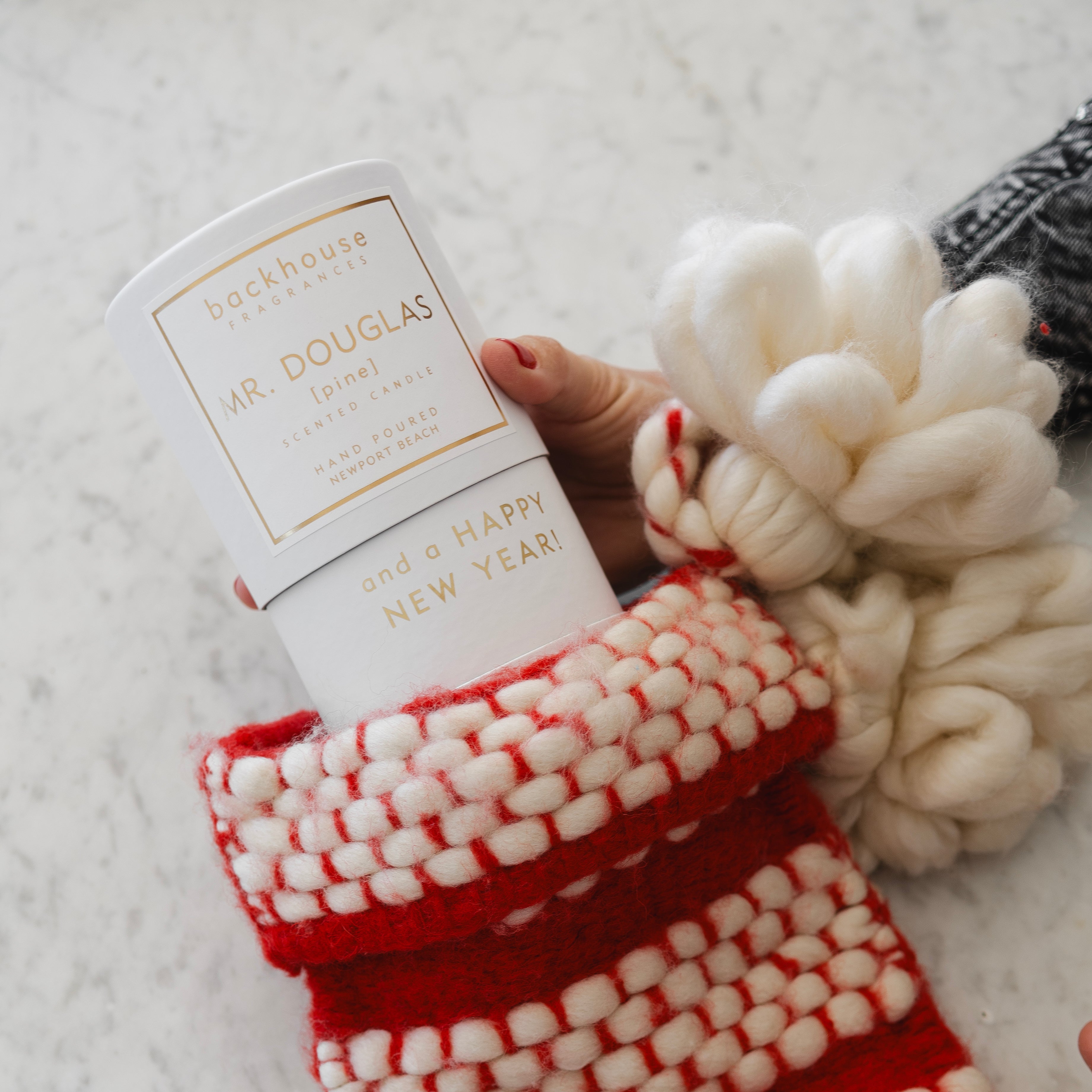 Red and white textured stocking with a hand holding a Douglas product against a light background