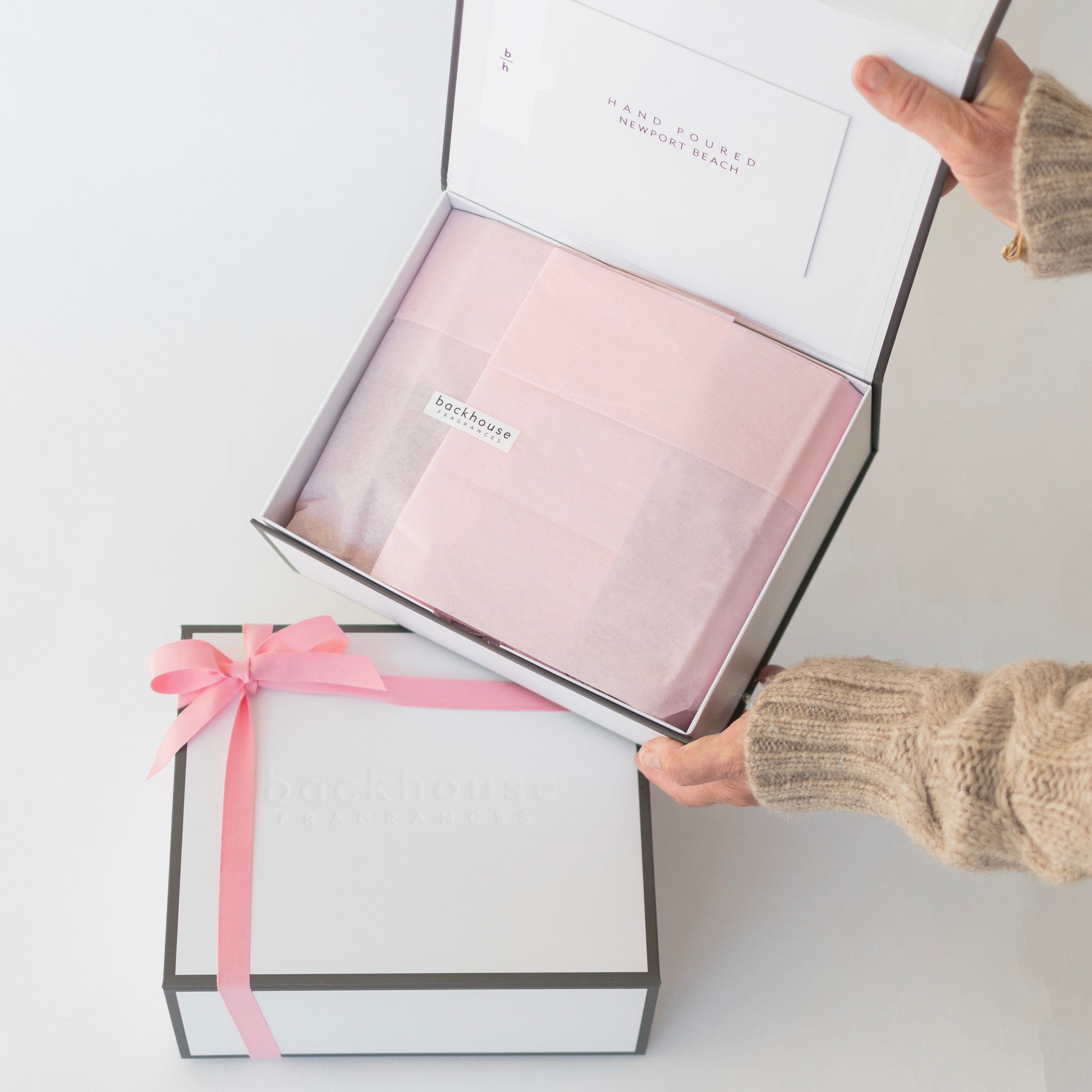 Person opening a gift box with pink tissue paper and ribbon