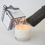 Backhouse Fragrances large hurricane candle with three lit wicks beside a closed gift box with herringbone ribbon
