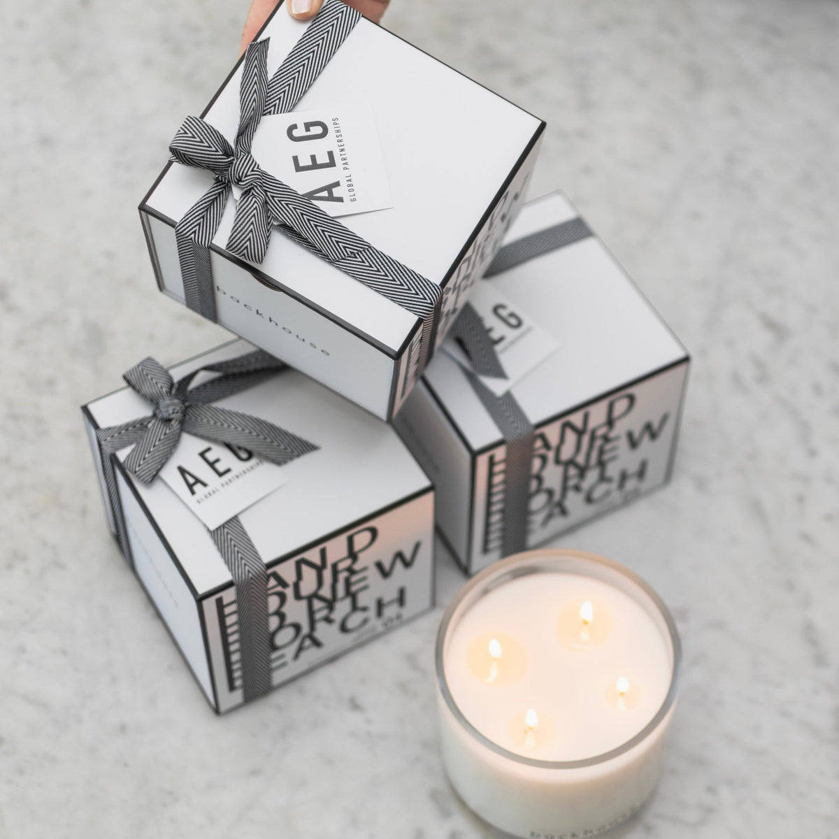 Backhouse Fragrances AEG Global Partnerships branded corporate gift boxes with herringbone ribbon on marble surface