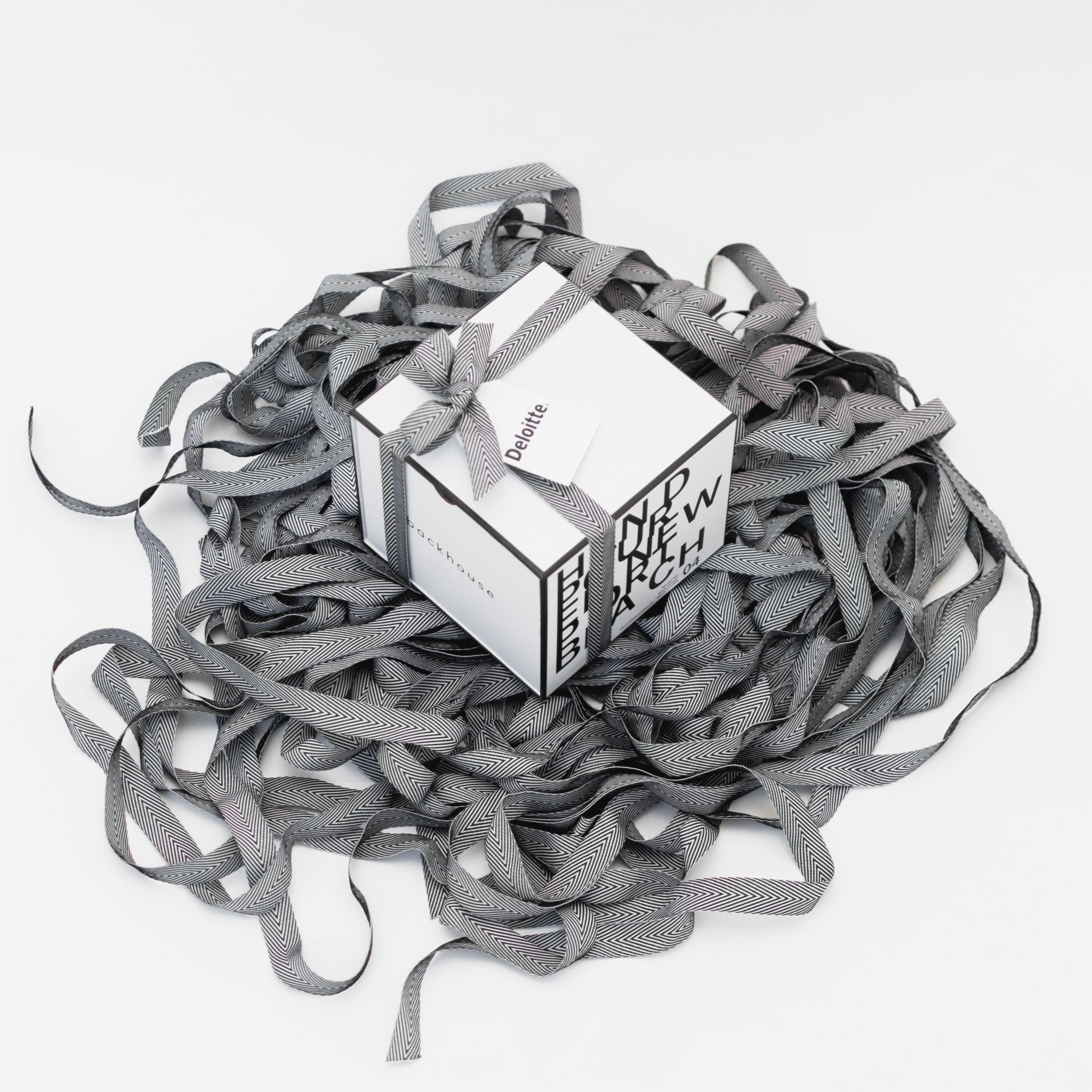 Backhouse Fragrances Deloitte branded corporate gift box tied with herringbone ribbon, nestled in a pool of signature ribbon on white background