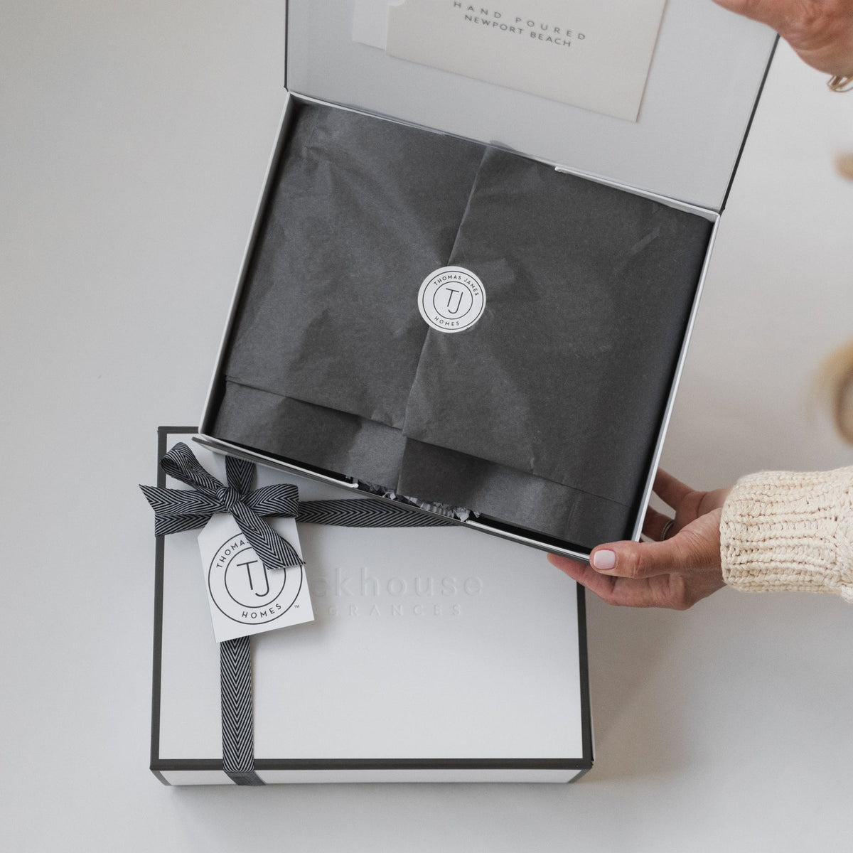 Backhouse Fragrances corporate gift box with Thomas James Homes branded tag and herringbone ribbon being opened