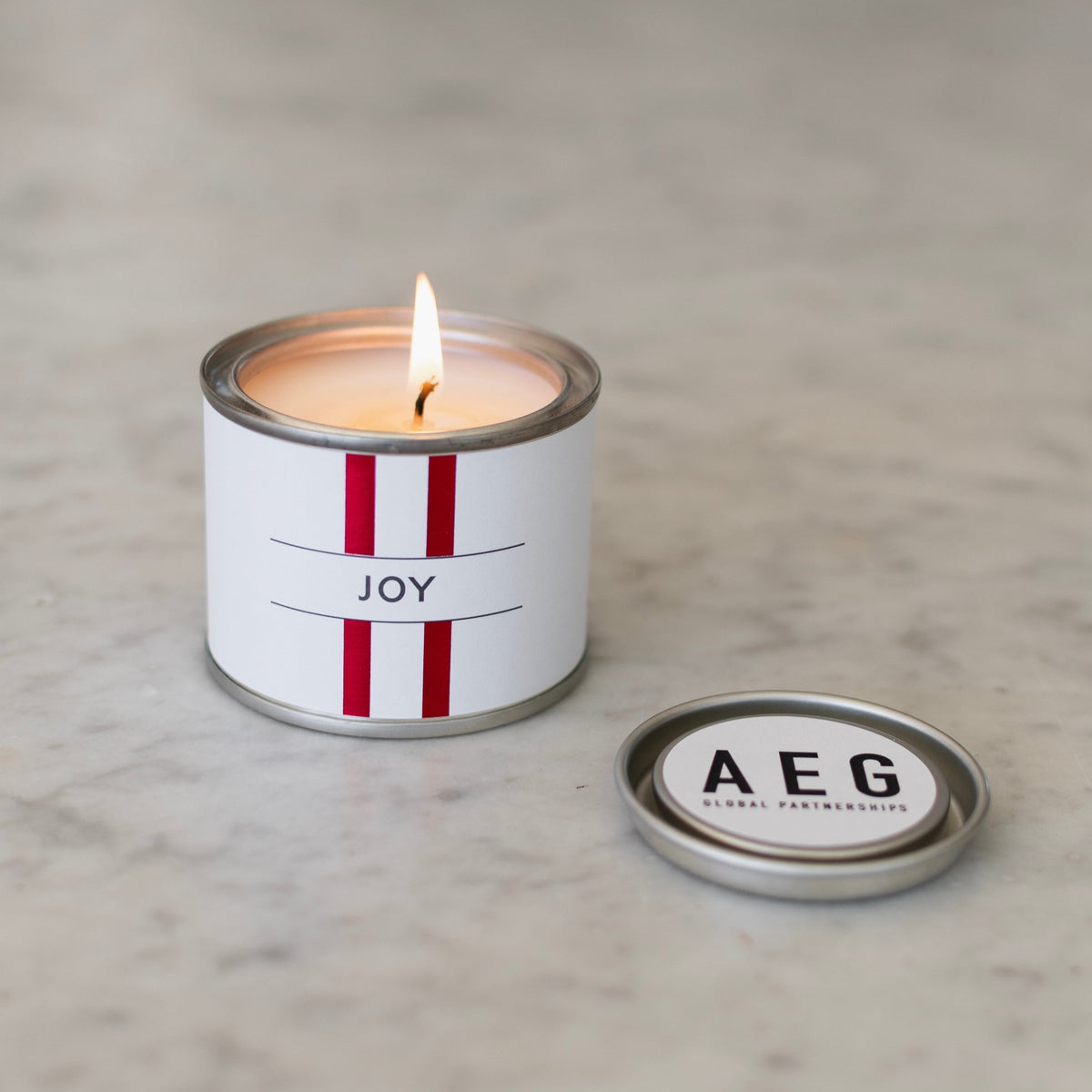 Lit Backhouse custom mini candle with a red striped Joy label beside a lid with a branded logo sticker on marble