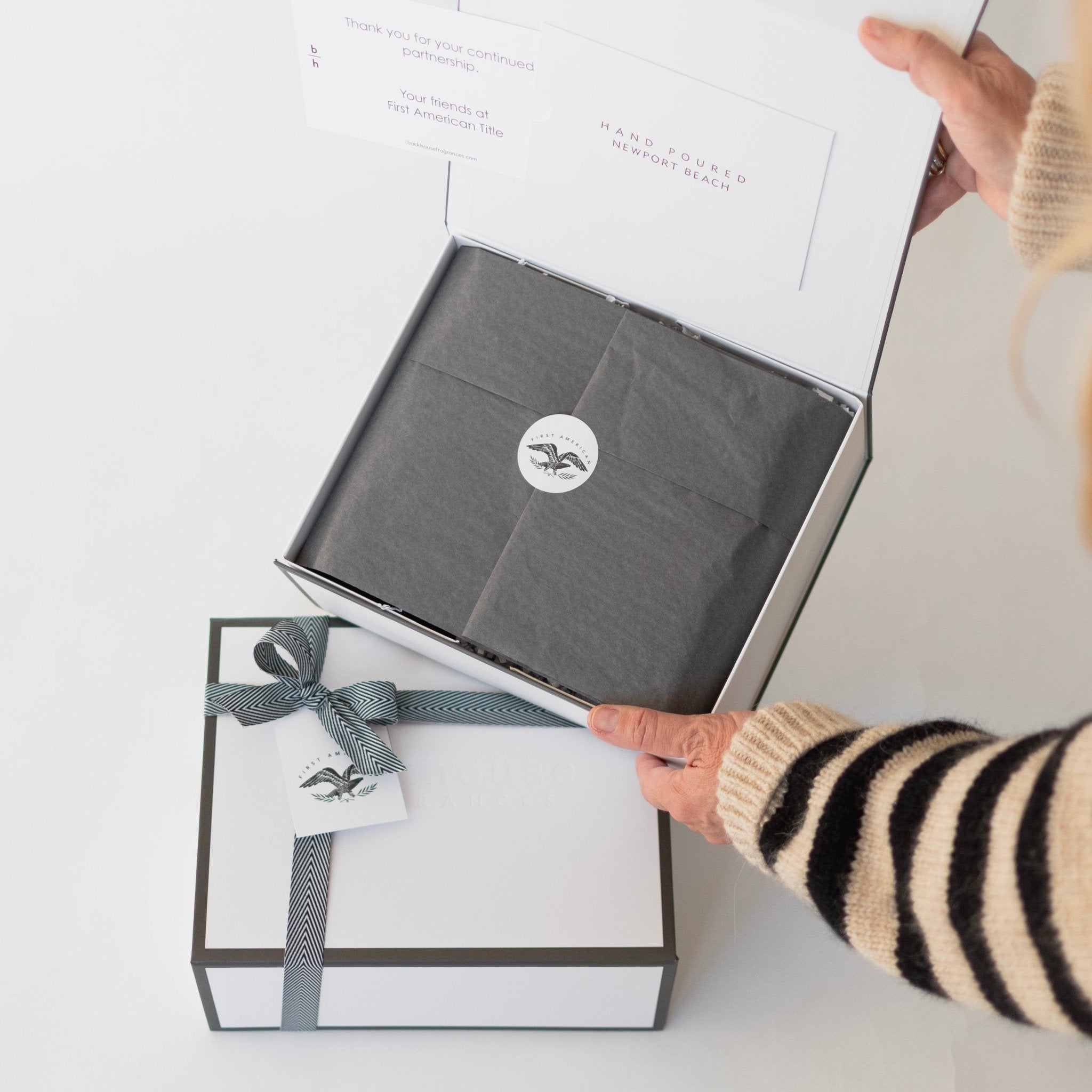 Backhouse Fragrances corporate gift box for First American Title being opened, with herringbone ribbon and branded tissue paper