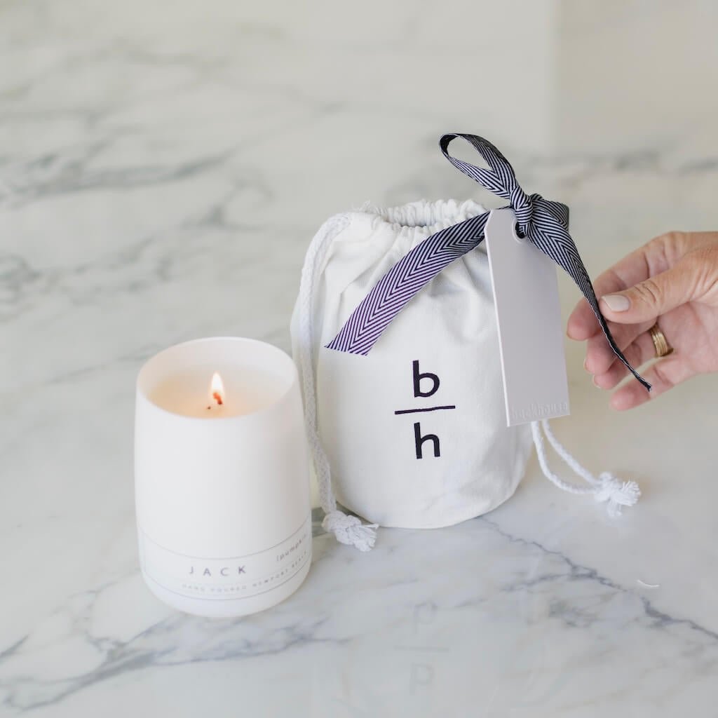 White candle and white drawstring bag with 'b/h' text on a marble surface