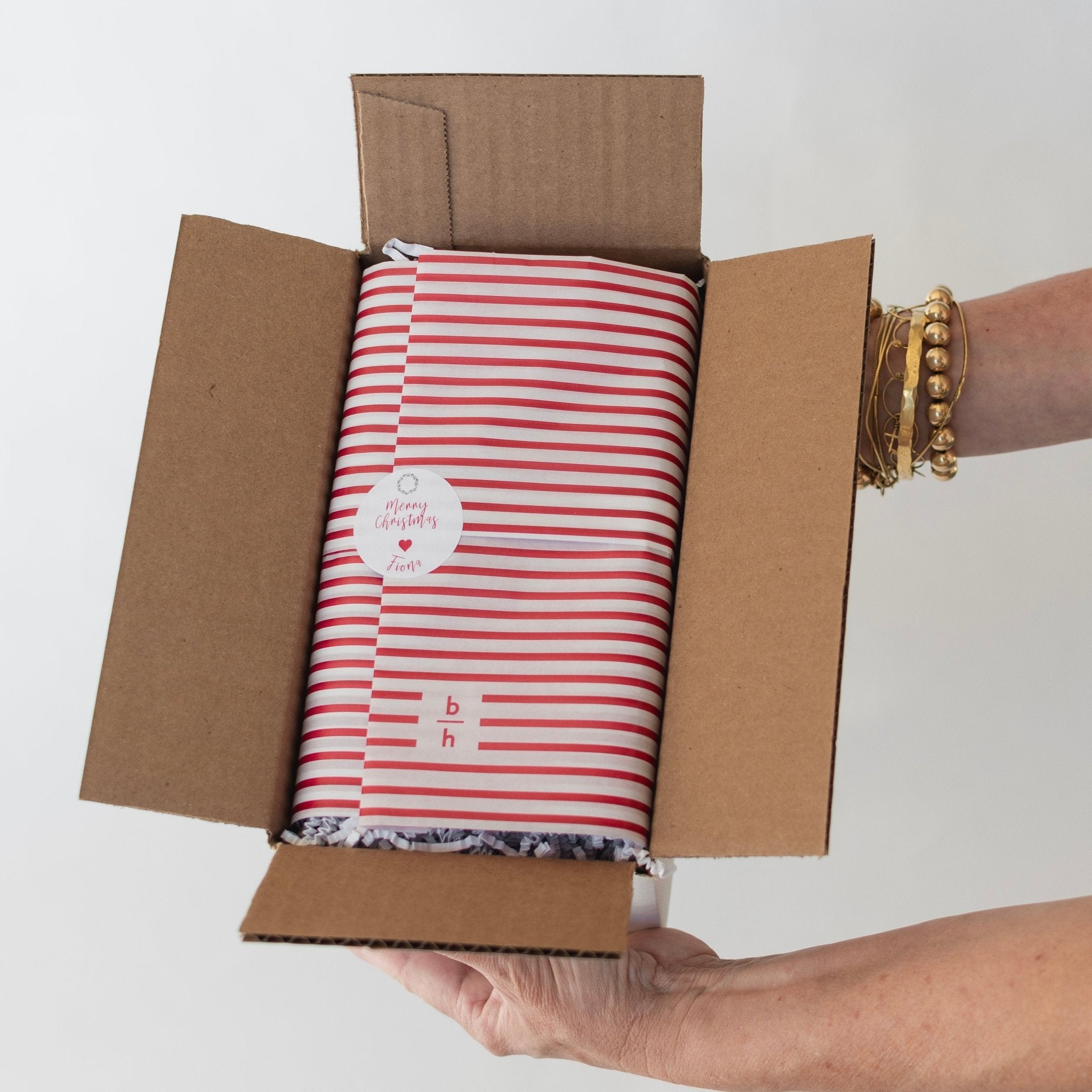 Person holding a cardboard box with a red and white striped product inside.