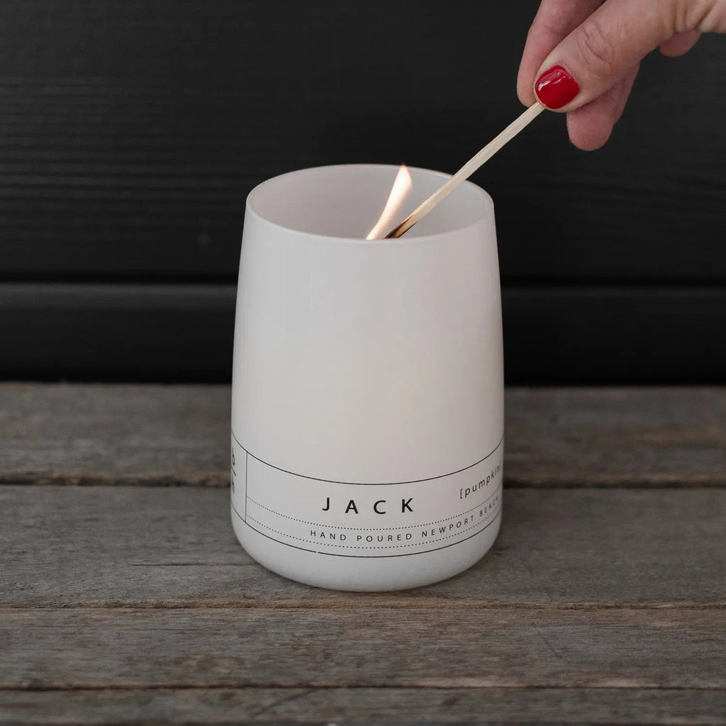 Hand lighting the Jack pumpkin candle by backhouse against a dark background.