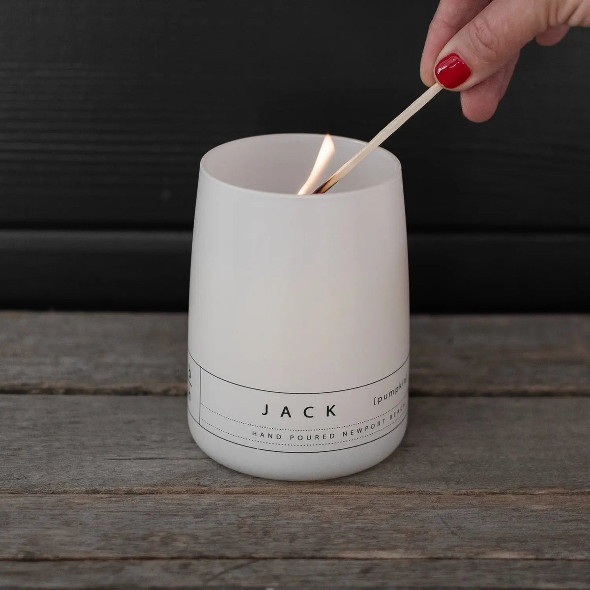 Hand lighting the Jack pumpkin candle by backhouse against a dark background.