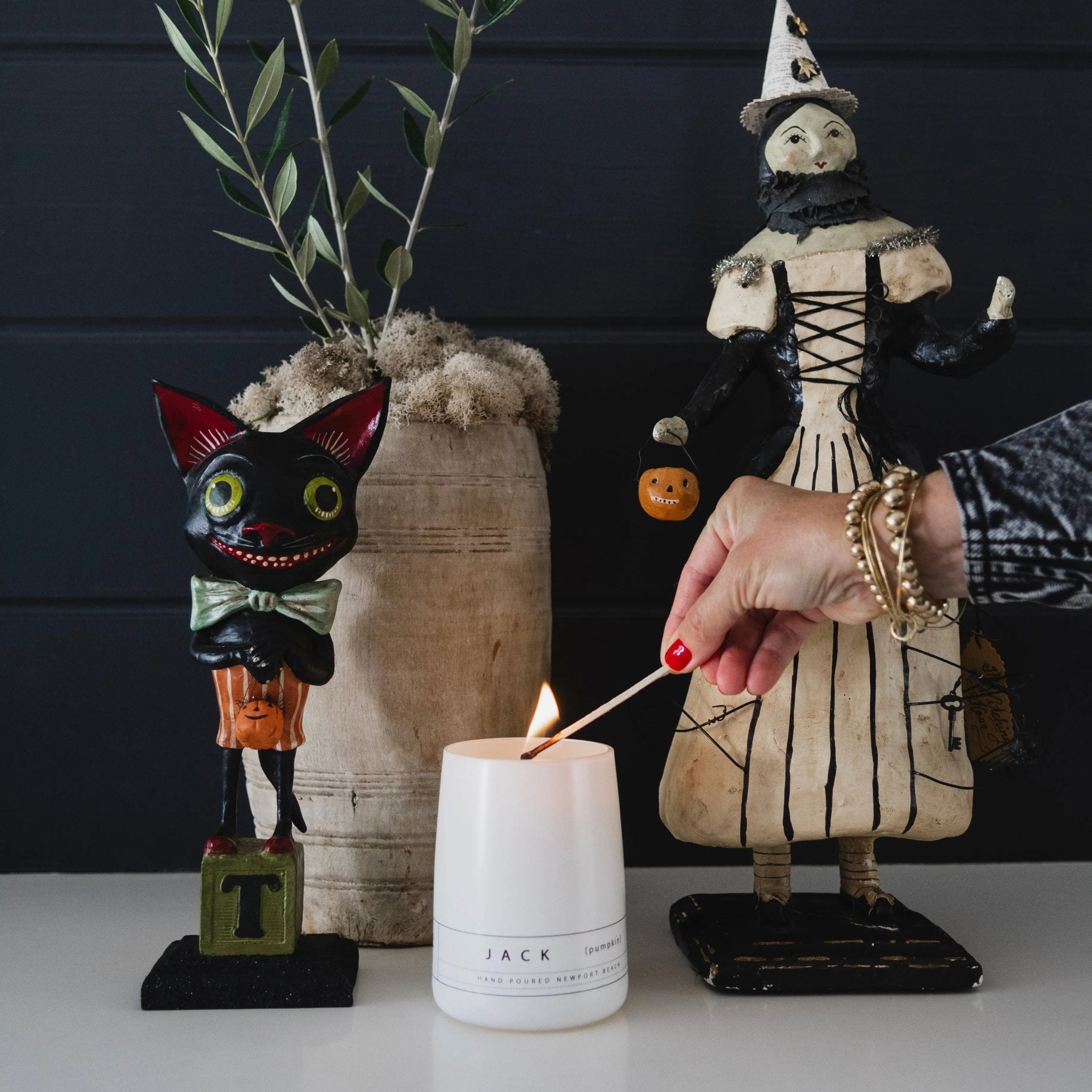 Jack pumpkin candle by backhouse burning beside decorative figures in a styled setting.