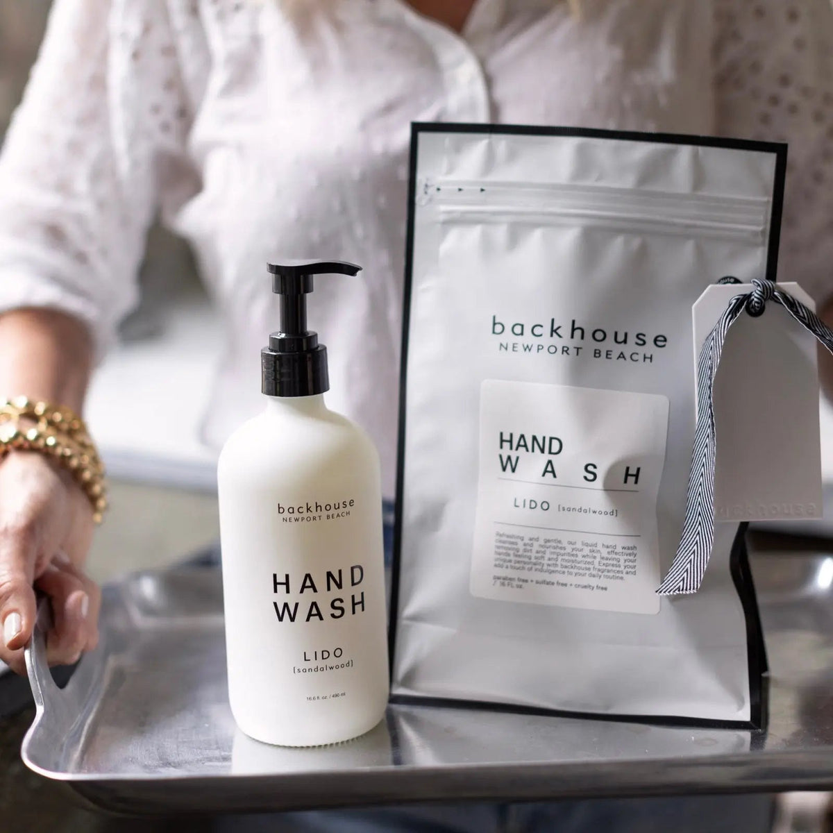Hands holding a silver tray with the Lido sandalwood hand wash by backhouse, with its custom coffee bag packaging in the background.