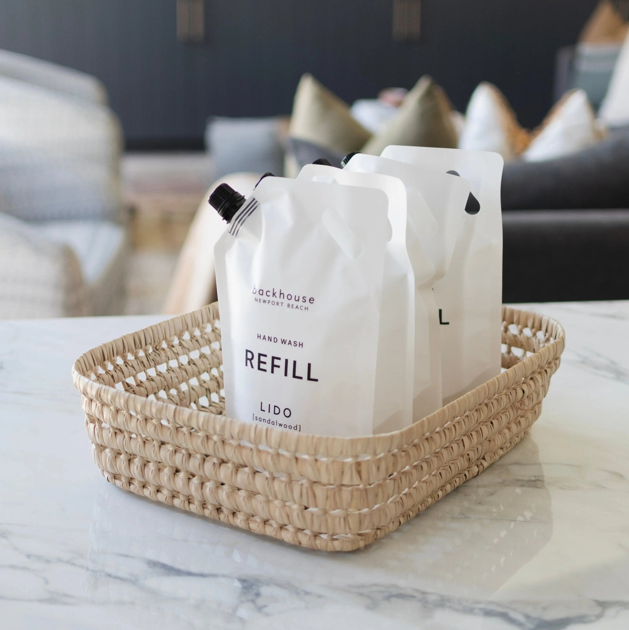 Lido sandalwood 32oz hand wash refill pouch by backhouse displayed in a woven basket on a marble surface.