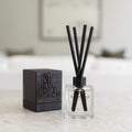 Backhouse Newport Beach LIDO reed diffuser, sandalwood scent, in a clear glass bottle with black reeds and gift box on a marble countertop.