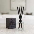 Backhouse Newport Beach LIDO reed diffuser, sandalwood scent, in a clear glass bottle with black reeds and gift box on a marble countertop.