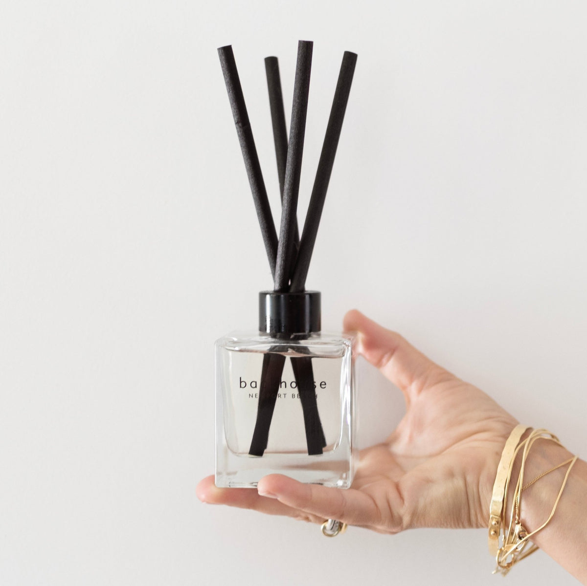 Backhouse Newport Beach LIDO reed diffuser held in hand to show size, sandalwood scent in a clear glass bottle with black reeds.