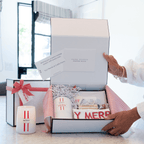 Person opening a gift box with festive items on a marble surface