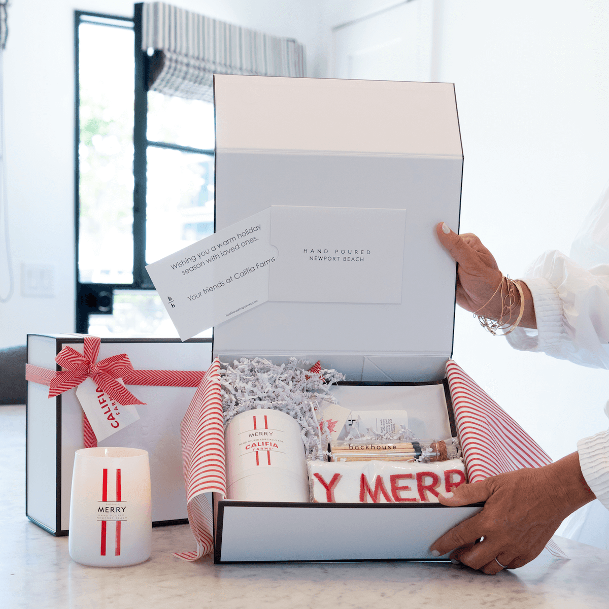 Person opening a gift box with festive items on a marble surface