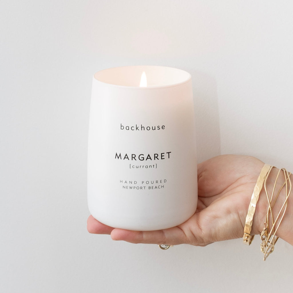 Hand holding lit Backhouse Fragrances Margaret currant scented candle, hand-poured luxury home fragrance in Newport Beach California