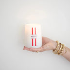 Hand holding the Merry Mr. Douglas pine candle by backhouse against a white background in a classic glass vessel.
