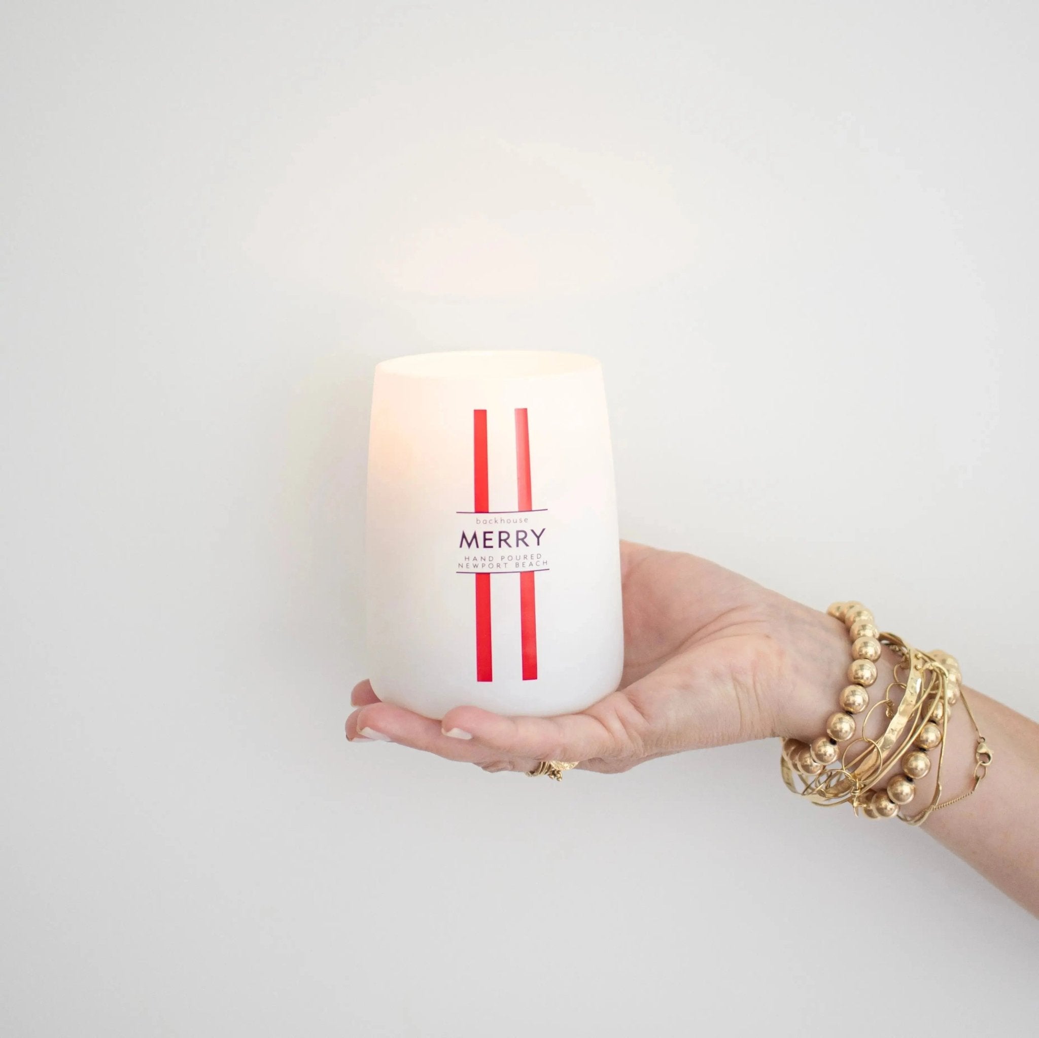 Hand holding the Merry Mr. Douglas pine candle by backhouse against a white background in a classic glass vessel.
