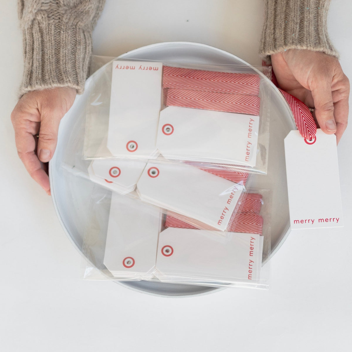 Merry merry hangtags displayed on a platter with a person holding a hangtag in their hand. Gifting hangtags. 