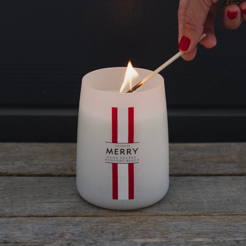 Hand lighting the Merry Mr. Douglas pine candle by backhouse against a dark background.