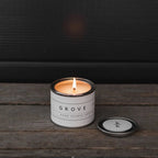 Mini Grove orange blossom candle by backhouse burning against a dark background in its classic glass vessel.