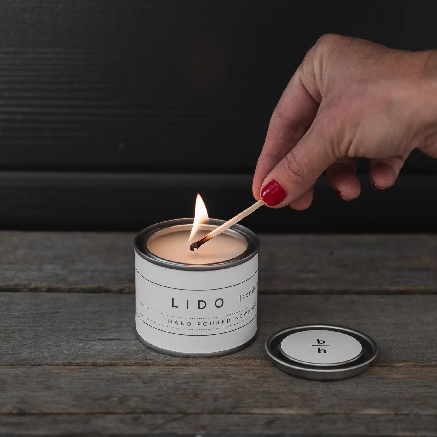 Hand lighting the Mini Lido sandalwood candle by backhouse with a match against a dark background.
