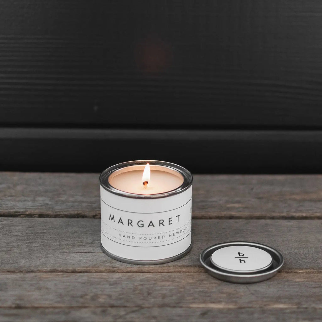 Mini Margaret currant candle by backhouse burning on a wood surface with the metal lid placed beside it.
