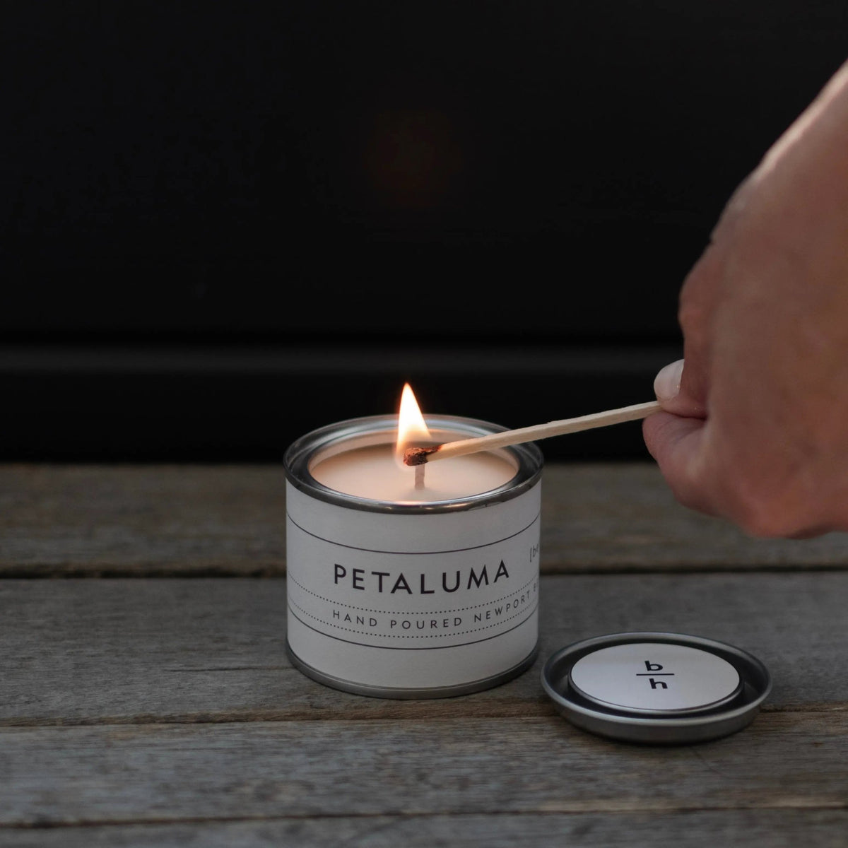 Mini Petaluma berry candle by backhouse being lit with a match against a dark background.